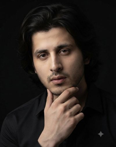 Dark-haired man in a black shirt poses against solid background