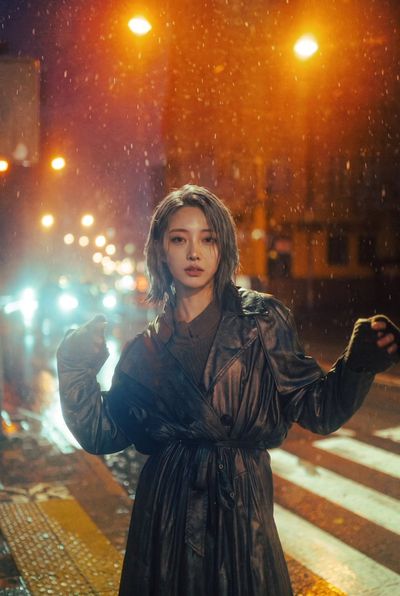 Young Woman in Black Trench Coat Stands in Rainy Night Portrait