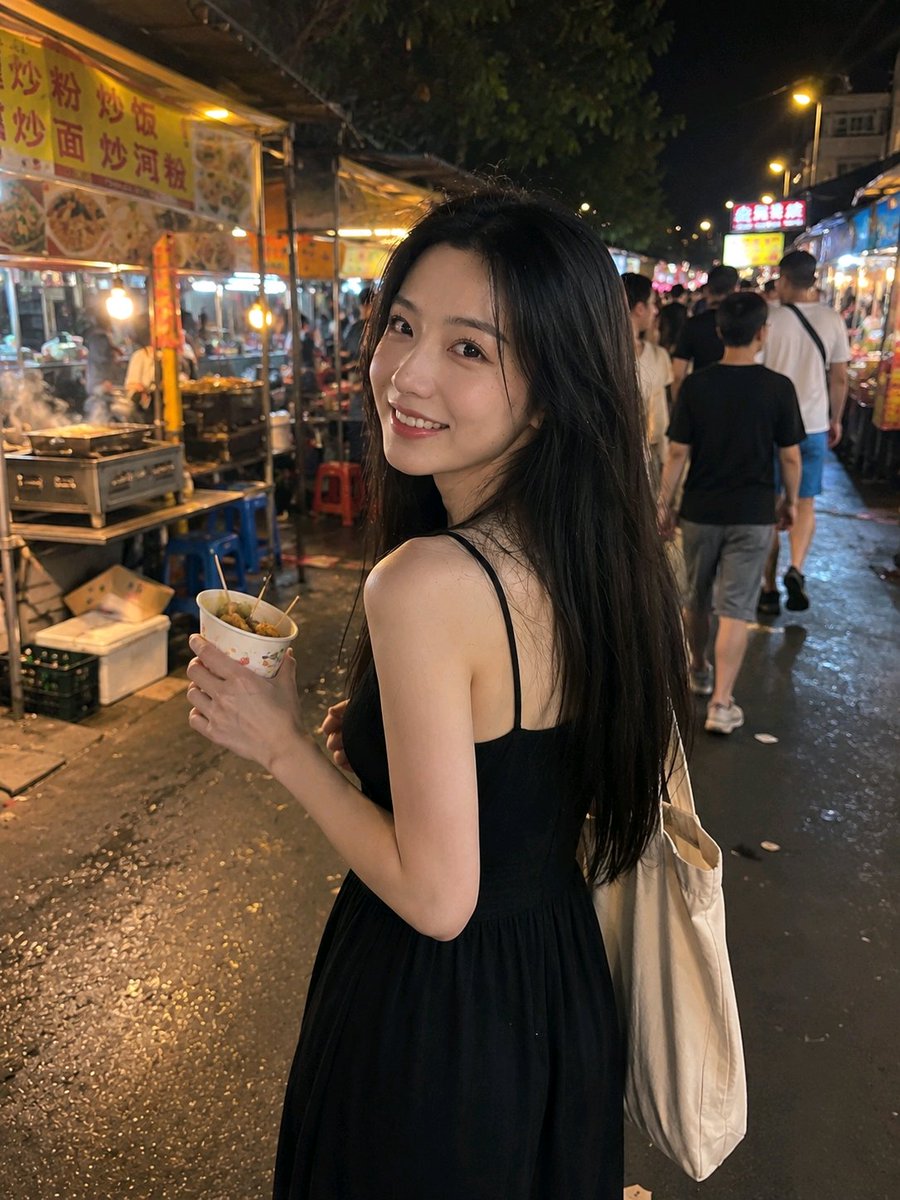 A woman in a black dress turns smiling at night market stalls