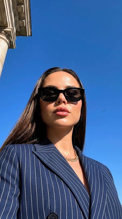 A woman in a navy blazer poses against a cobalt sky.