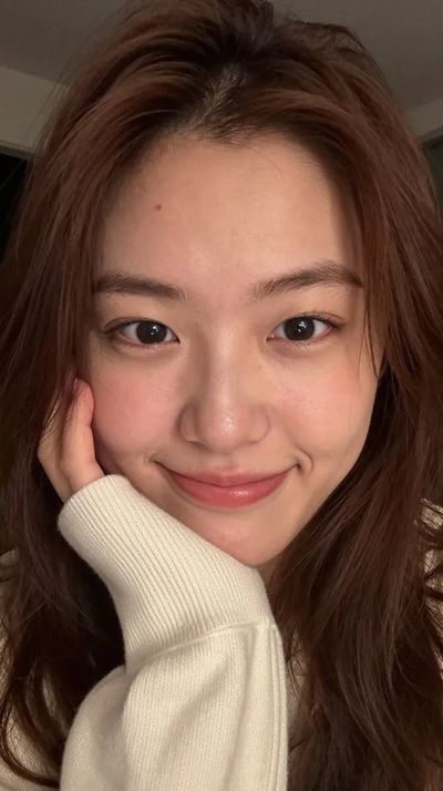 Young East Asian woman rests cheek on hand in warm portrait