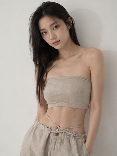 Young woman in oat top and linen pants gazes away in soft studio light