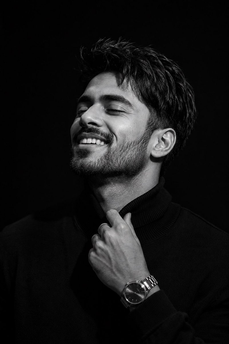 A man in black turtleneck smiles softly under dramatic light