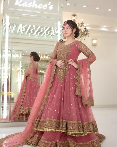 A bride in an embroidered pink gown poses inside a luxurious boutique