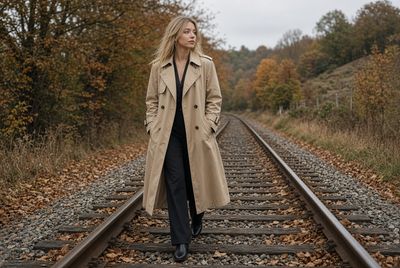 Blonde woman in trench coat walks along autumn railway tracks