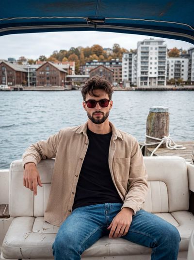 Young man in beige corduroy sits aboard weathered white boat