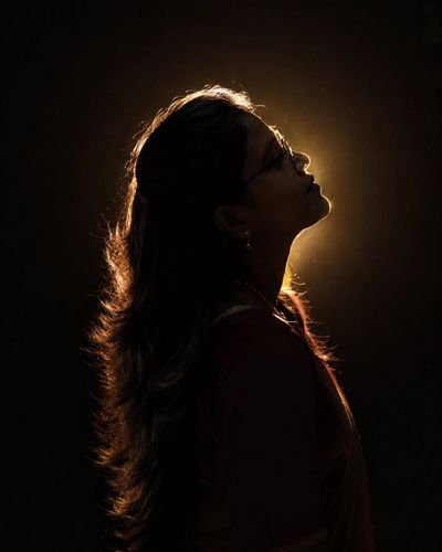 A woman in profile tilts back toward a warm glowing light.