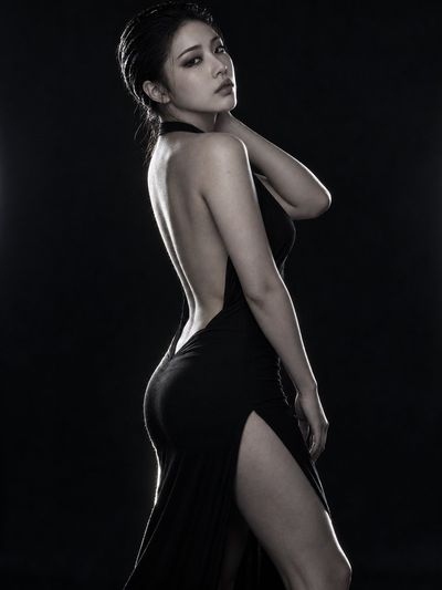 Elegant East Asian Woman in Black Dress Poses Against Dark Studio