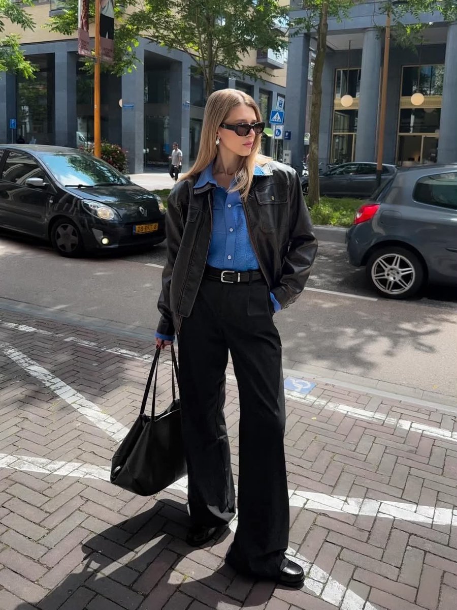 Stylish woman in leather jacket walks sunlit European street casually