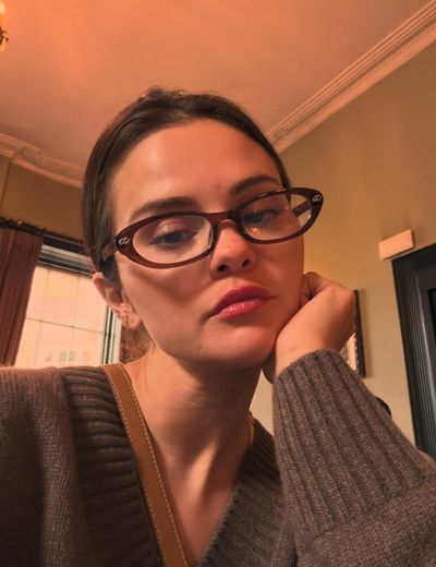 Young woman in tortoiseshell glasses rests chin on hand thoughtfully