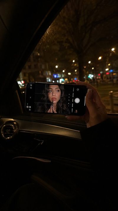A woman holds an iPhone showing her face in a dark car