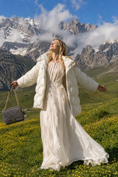 Blonde woman in white dress stands in alpine meadow under sun