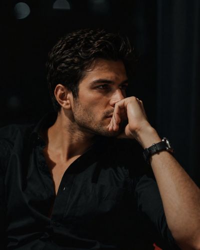 A pensive man in a black shirt sits alone in a dim lounge