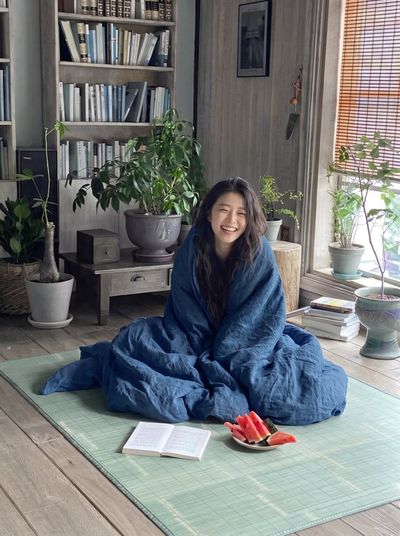 Joyful Woman Wrapped in Orange Duvet Laughs on Tatami Mat
