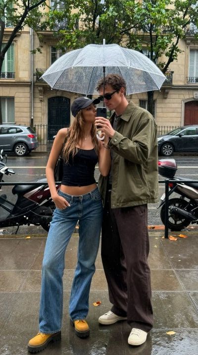 Couple shares a rainy kiss in a mirrored storefront reflection