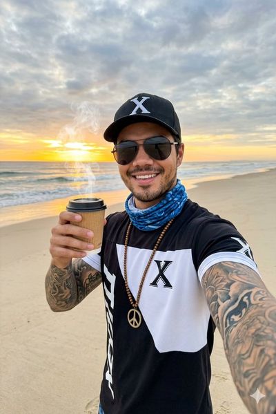 Tattooed man smiles with coffee at sunrise on beach