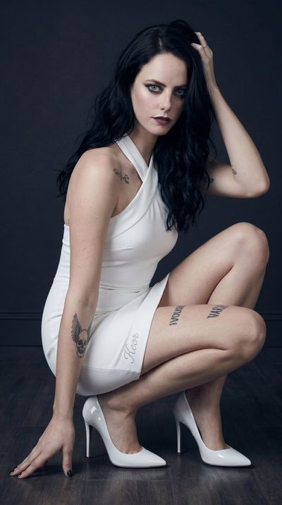 Young woman in white dress poses confidently against dark backdrop