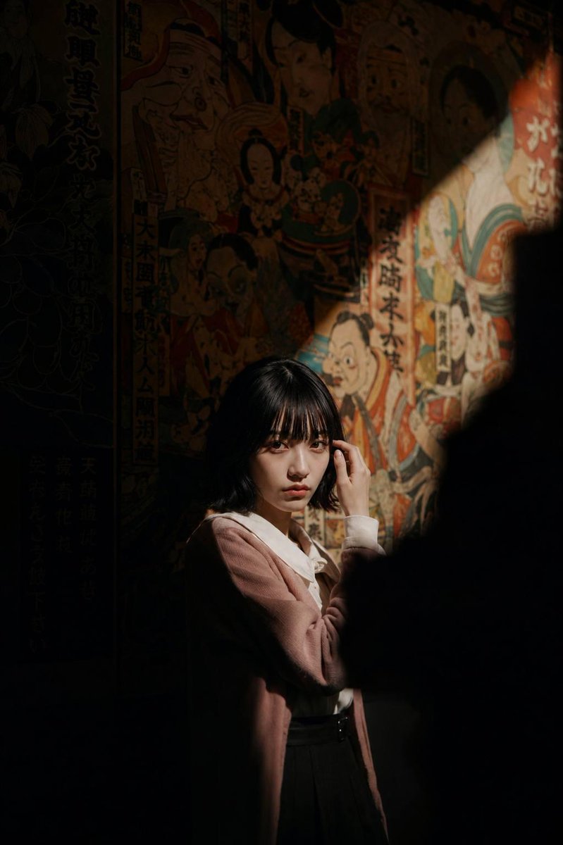 Woman in vintage jacket stands in dark room with mural
