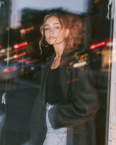 A confident woman in a charcoal blazer stands before a glowing storefront