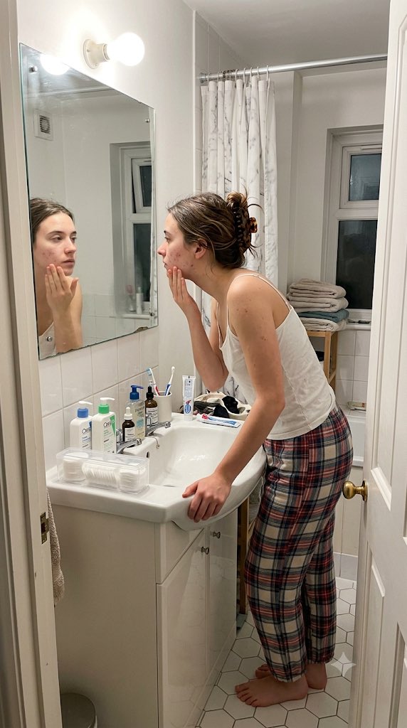 Young woman applies moisturizer in harsh bathroom light captured candidly