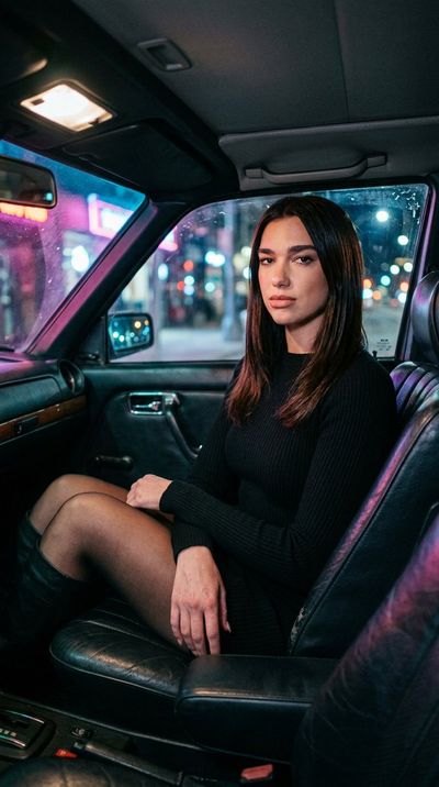 Dua Lipa poses in a dim car with phone light glowing