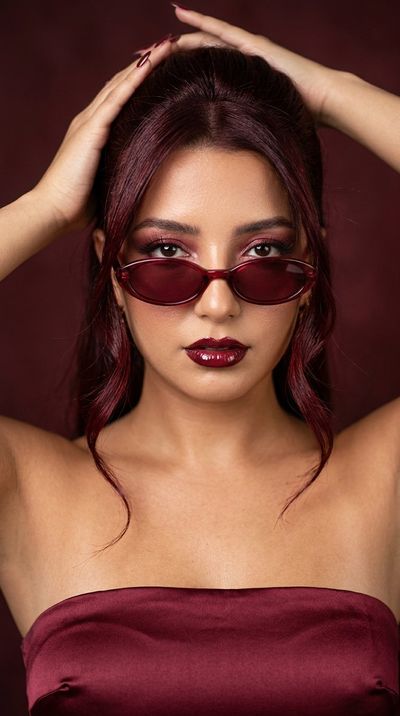 Woman in wine-red glasses sweeps back glossy hair in editorial shot