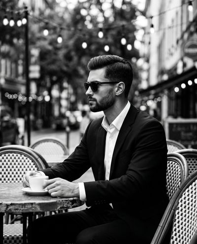 Stoic man in suit sips coffee at urban sidewalk cafe