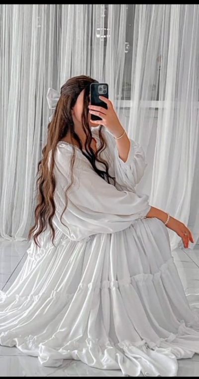 Young woman in white satin dress captures mirror selfie on marble floor.