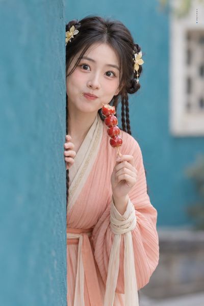 Hanfu girl peeks from teal wall with tanghulu in hand