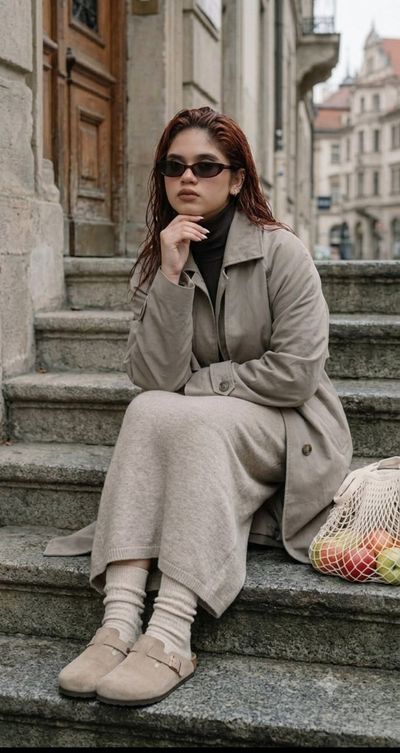 Woman in oversized trench coat sits on steps with apples