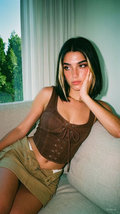 A woman with dark hair and heavy makeup sits on a beige sofa