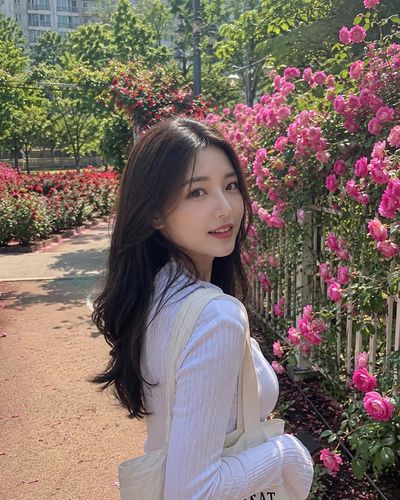 Young woman with dark hair glances back in sunny rose garden