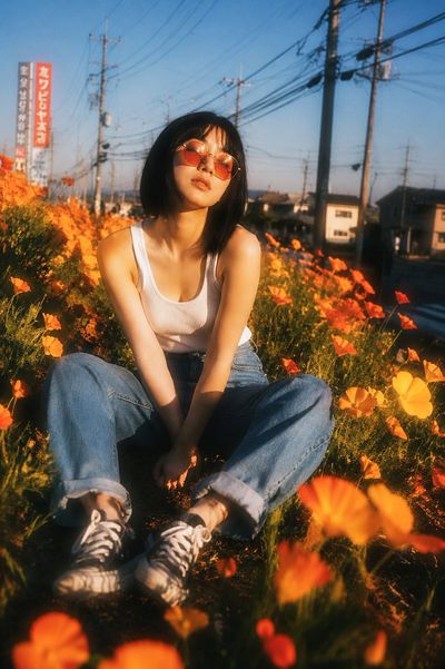 A woman in a white tank top sits among orange poppies at golden hour.