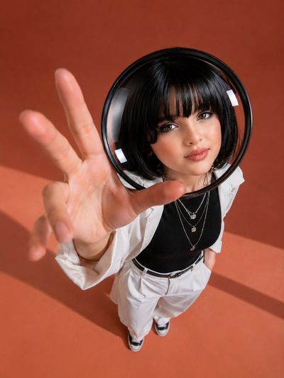 A woman in a black bob extends her hand upward through a magnifying lens