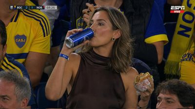 Glamorous woman enjoys burger and drink at a night football game.