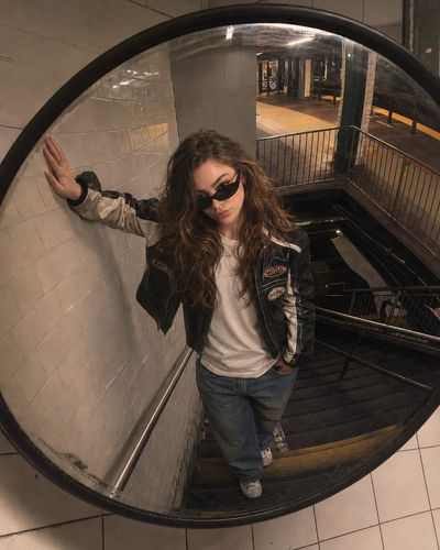 A woman in a leather jacket gazes into a curved security mirror.