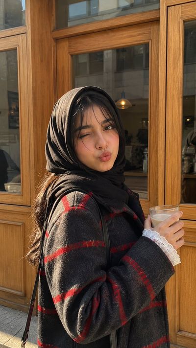 A young woman winks playfully while holding a latte outside a cozy café