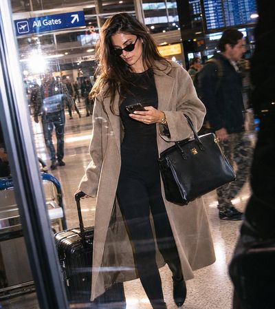 A stylish woman walks through an airport terminal in an oversized coat