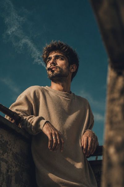 A mysterious young man leans against concrete railing with cigar smoke