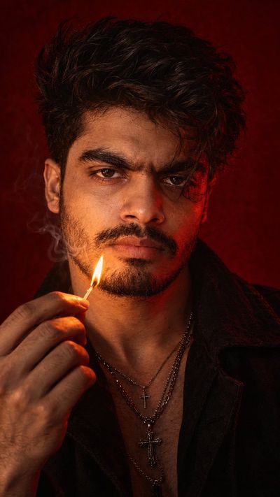 Intense young man holds a lit match against deep crimson backdrop