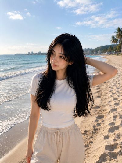 A Korean woman sits on warm sand during golden hour sunset.