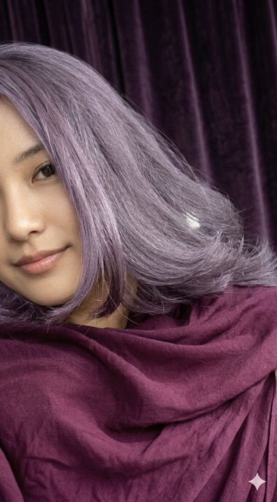 Woman with lavender hair smiles softly in purple velvet light