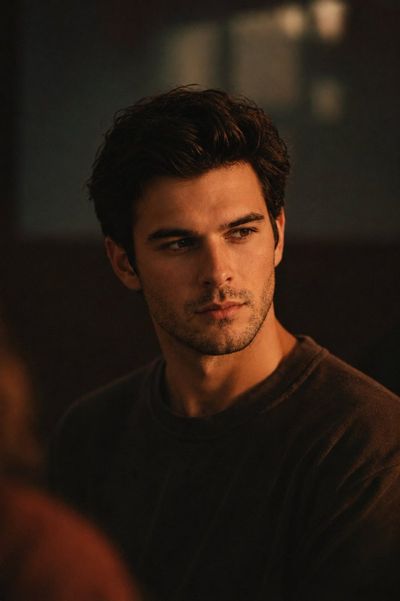 A handsome young man sits calmly in warm amber cinematic light