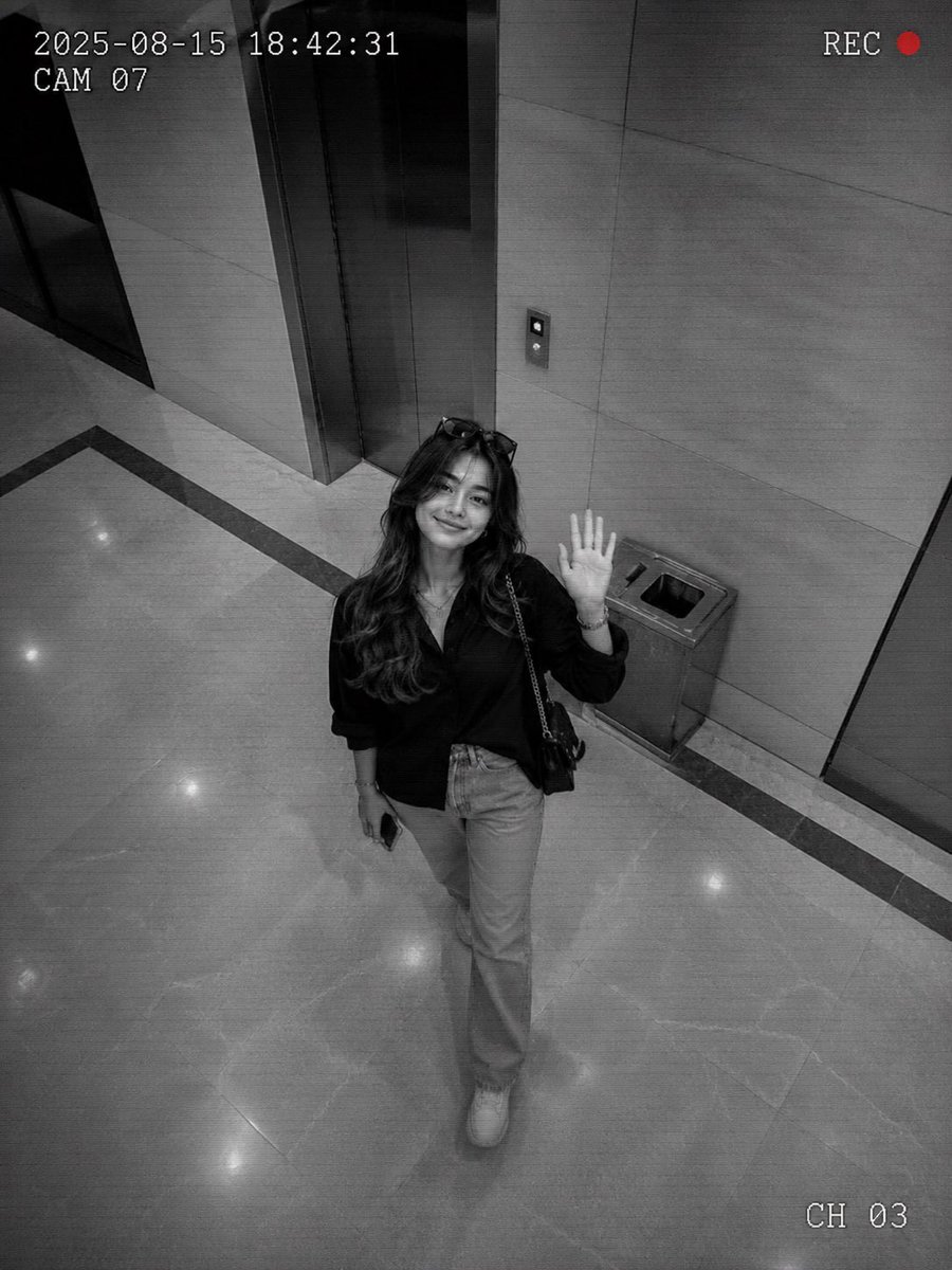 Man in lobby waves at ceiling camera in grainy monochrome