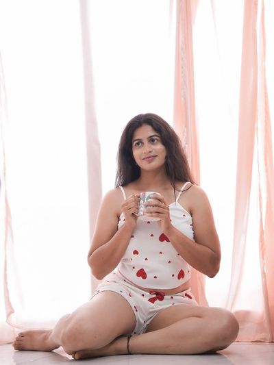 Woman with a white mug sits cross-legged in soft sunlight