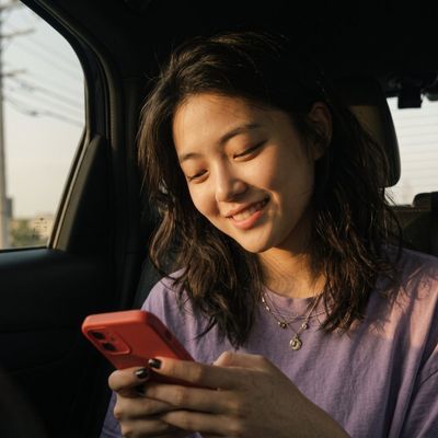 Cinematic portrait of a smiling woman texting in a sunlit car backseat