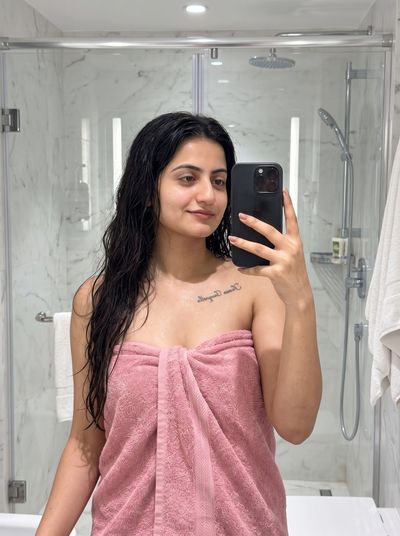 Woman with wet hair in pink towel smiles softly in marble bathroom