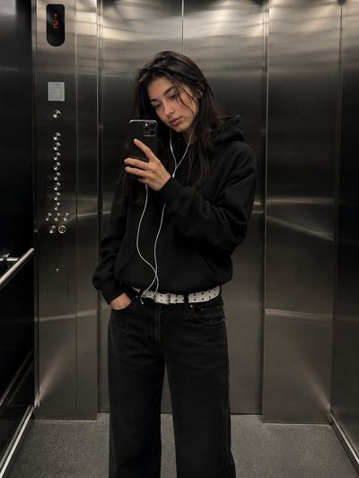 A stylish woman captures a confident mirror selfie inside a modern elevator