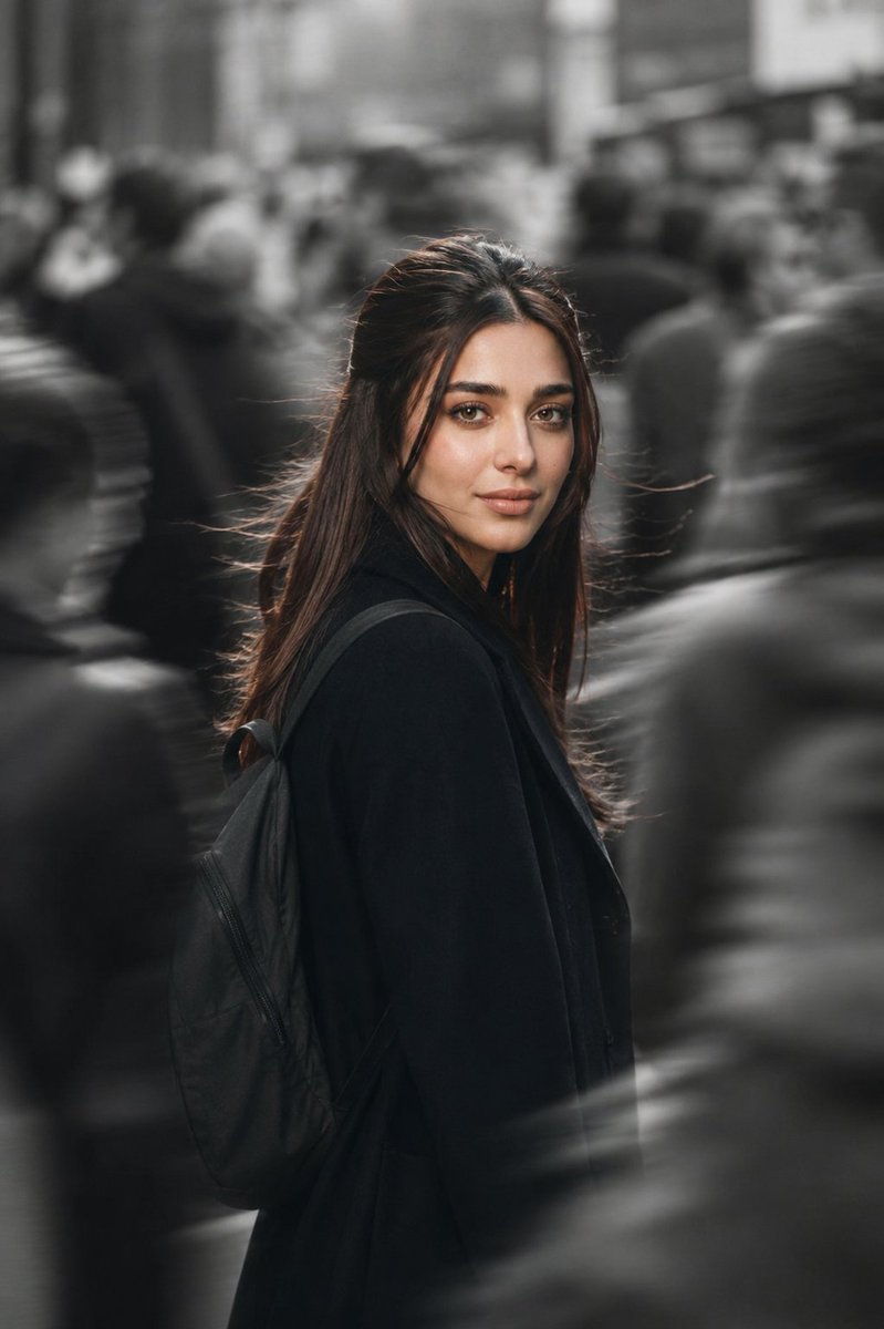Woman in black coat pauses amid blurred city crowd