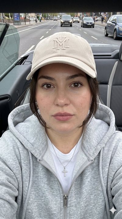 Model in beige cap and gray hoodie gazes calmly at camera